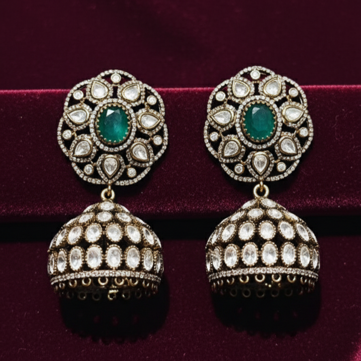 Noor Emerald Jhumkas earrings featuring vibrant emeralds and intricate designs on a velvet background.